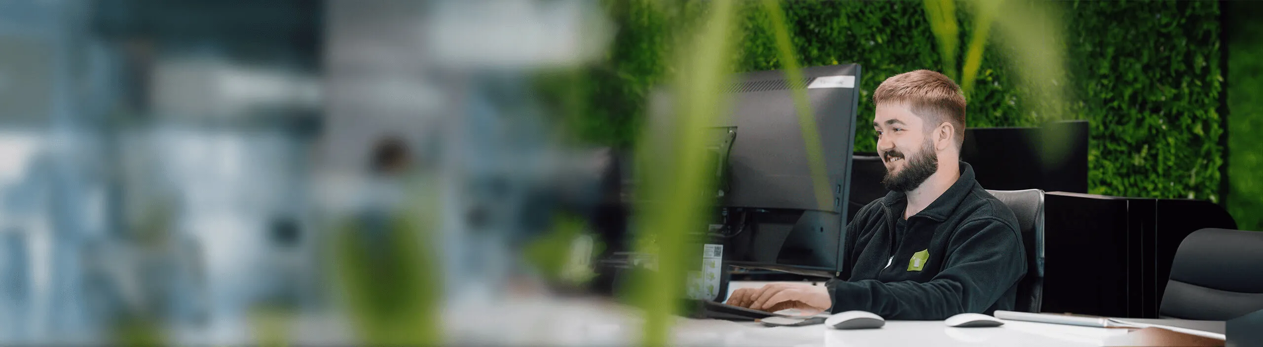 Man smiling at a computer in an office with a plant wall