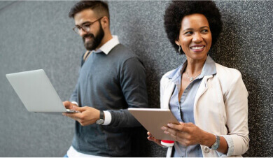 Close up of two people leaning against a wall, each holding a tablet and laptop